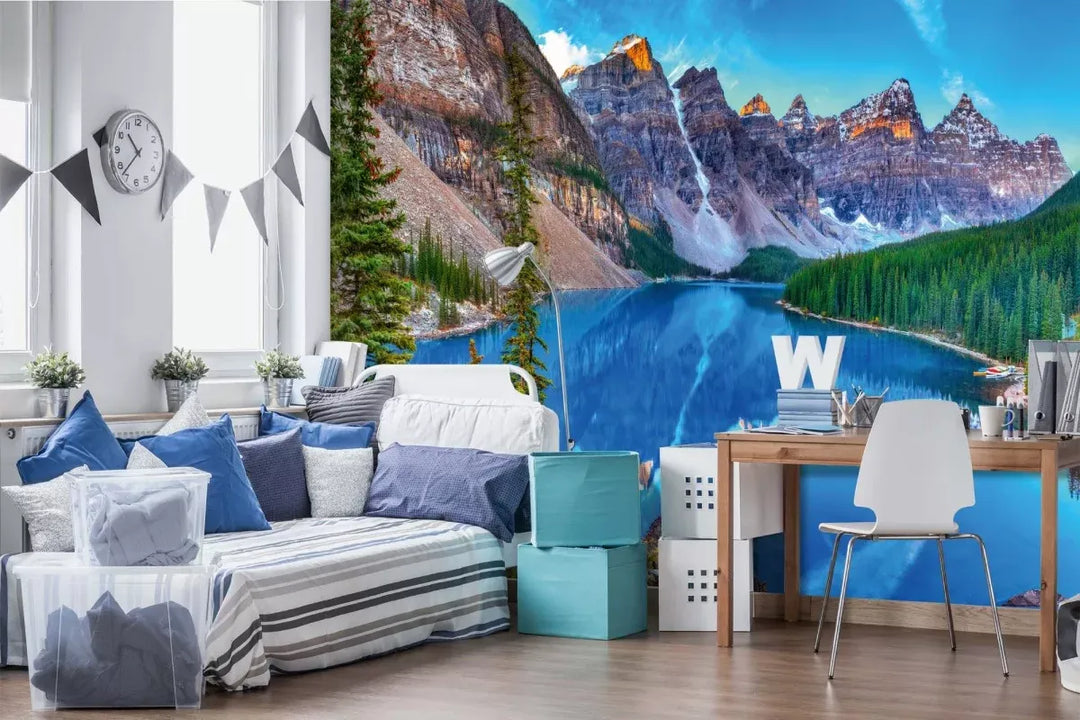 A room with a desk and a bed, decorated with photo wallpaper depicting a magnificent view of a mountain lake with bright turquoise water, against a backdrop of towering cliffs and a coniferous forest.