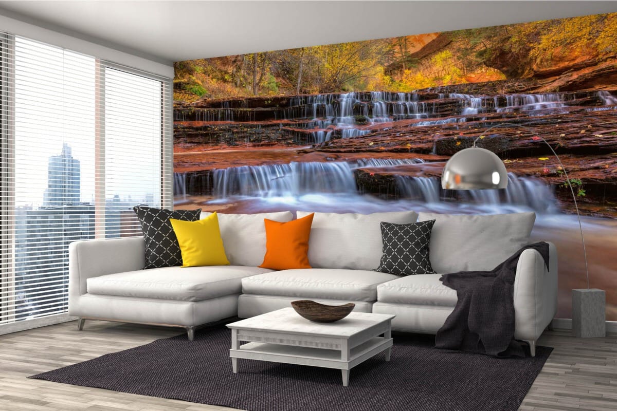 A modern living room with a white corner sofa and photo wallpaper depicting a picturesque cascading waterfall between red cliffs and an autumn forest.
