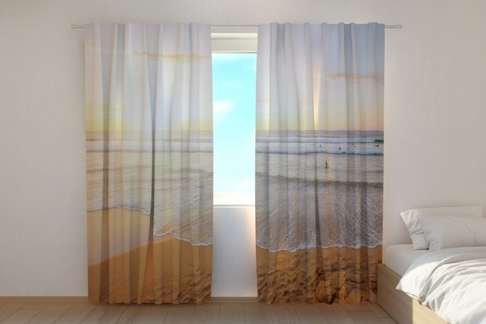 Gaišas guļamistsbas interjers ar koka grīdu un baltām sienām. Uz loga uzstādīti fotoaizkari, uz kuriem fotoreālistiski attēlota plaša un mierīga jūras piekraste saulrieta vai saullēkta zeltītajā gaismā. Priekšplānā redzamas smiltis un balti viļņi, kas vienmērīgi apskalo krastu. Fonā jūrā manāmi daži mazi sērfotāju silueti. 