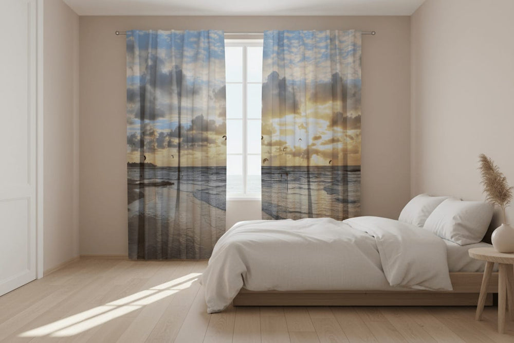 Gaišas guļamistabas interjers ar gaišu koka grīdu un lielu gultu. Uz loga uzstādīti fotoaizkari, uz kuriem fotoreālistiski attēlota okeāna piekraste saulrietā.