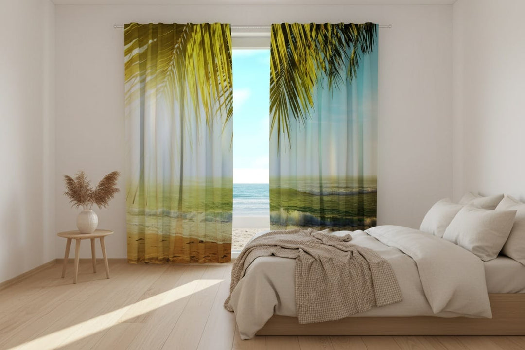 A bright bedroom interior with a large bed. Photo curtains are hung on the window, featuring a design dominated in the foreground by large, bright green and sunlit yellowish palm leaves hanging down from above.