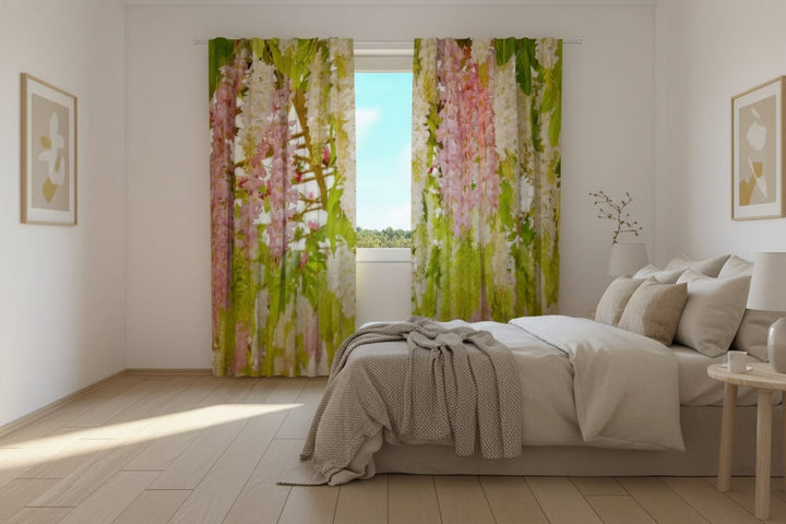 Gaišas guļamistabas interjers ar koka grīdu un lielu gultu gaišos toņos. Uz loga uzstādīti fotoaizkari, uz kuriem fotoreālistiski attēlots pavasarīgs dārza motīvs – bagātīgi, nokareni ķekari ar maigi rozā un baltiem ziediem (līdzīgi visterijām) un svaigi zaļām lapotnēm. 