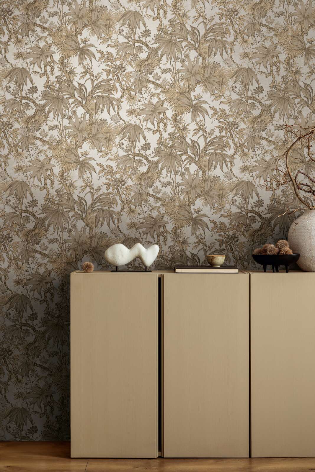 Beige botanical pattern wallpaper in an interior behind a beige dresser with decor and brown wood plank flooring