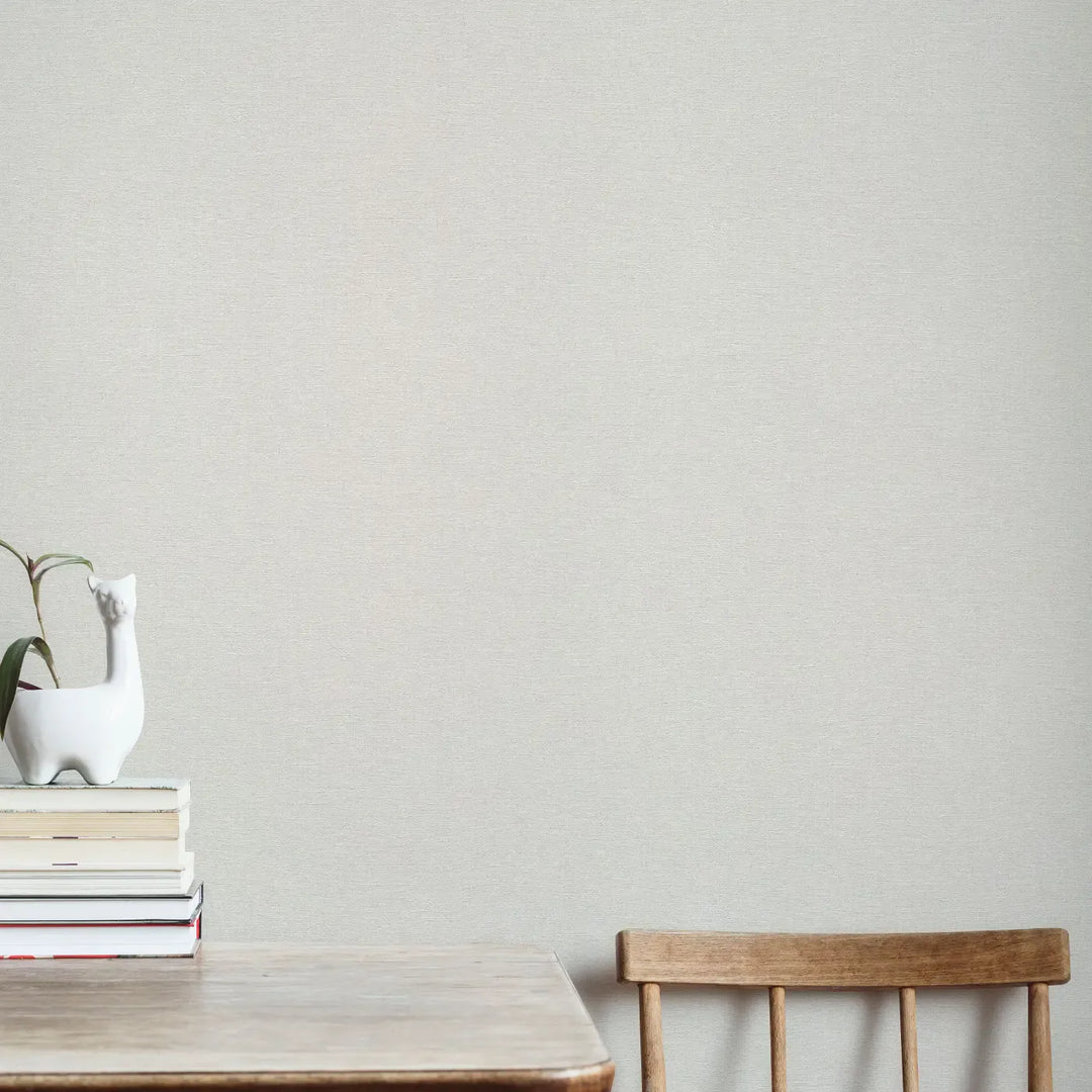Helehall peene kangatekstuuriga tapeet minimalistlikus interjööris valge põrandaga. Valgel disaintoolil on hall kootud pleed.