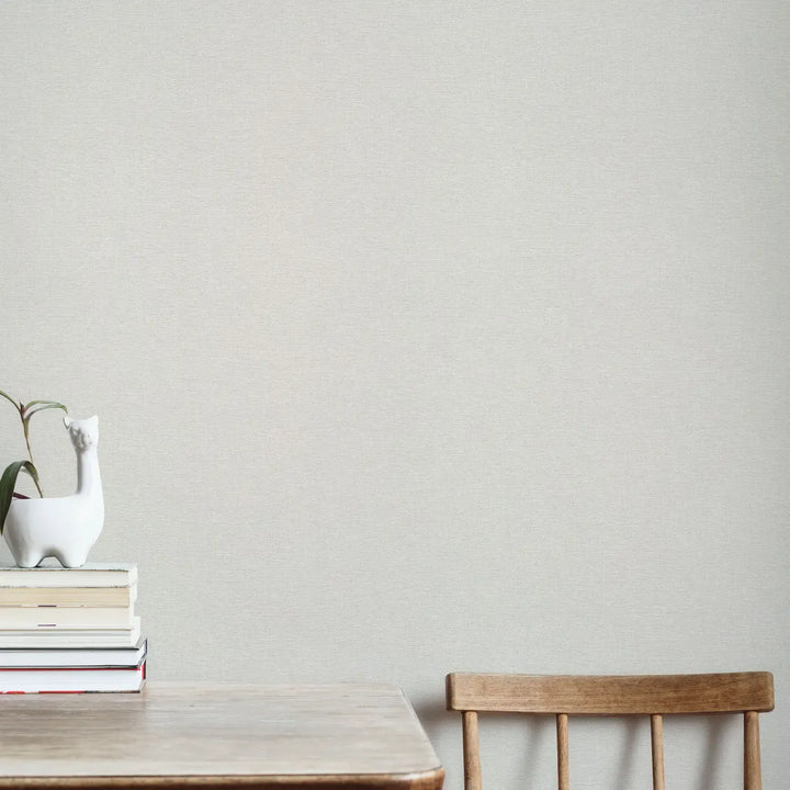 Helehall peene kangatekstuuriga tapeet minimalistlikus interjööris valge põrandaga. Valgel disaintoolil on hall kootud pleed.