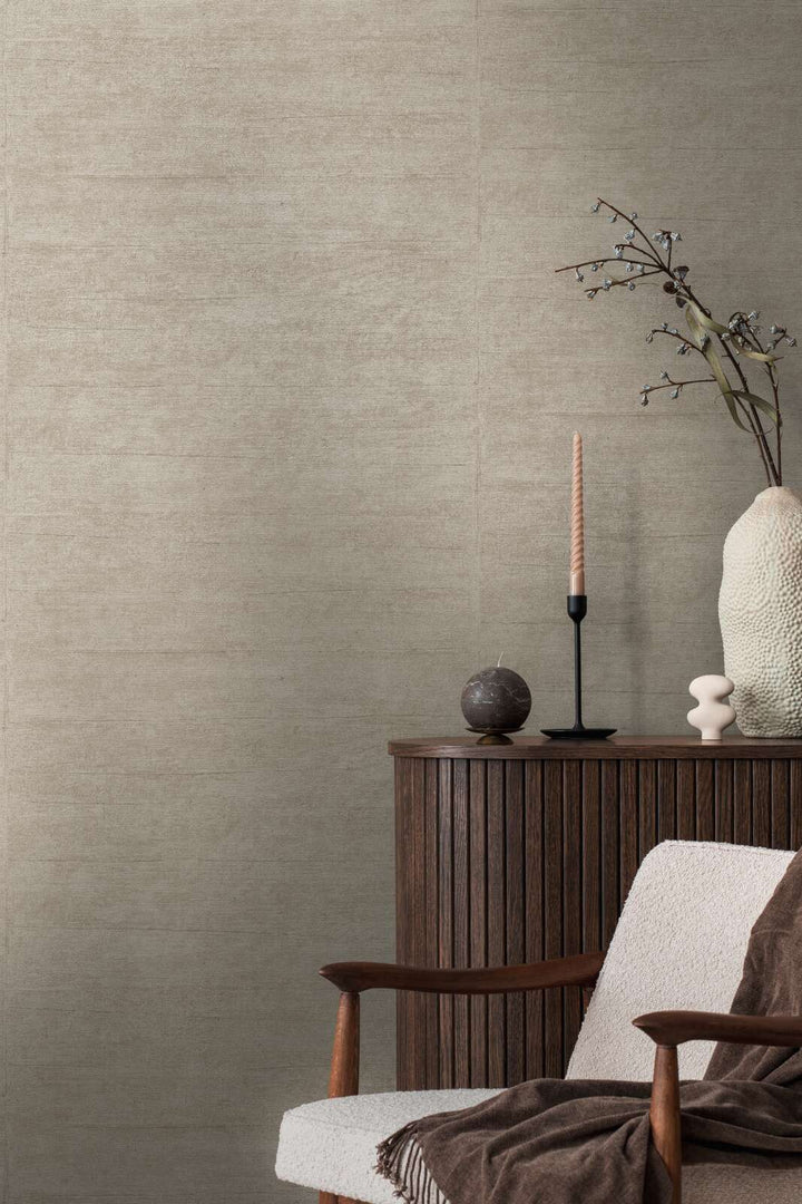 Grayish-brown textured wallpaper in an interior behind a wooden cabinet and lounge chair with decorative accents