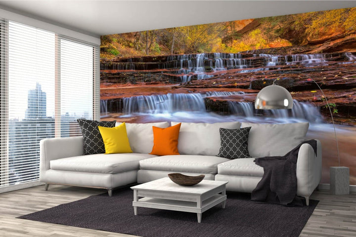 A modern living room with a white corner sofa and photo wallpaper depicting a picturesque cascading waterfall between red cliffs and an autumn forest.