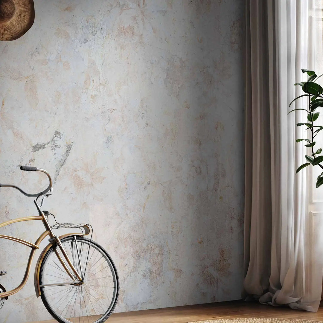 Photo wallpaper with a light floral motif and shabby concrete texture in an interior near a bicycle, window, and natural wooden plank floor with a rug