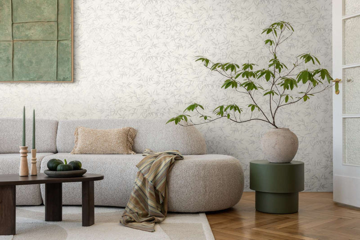 Light grayish-white bamboo leaf pattern wallpaper in a living room interior with a light sofa and natural wood parquet flooring with a light rug