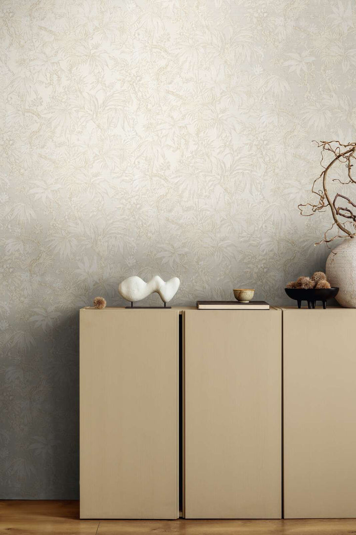 Light beige botanical pattern wallpaper in an interior behind a beige dresser with decor and brown wood plank flooring