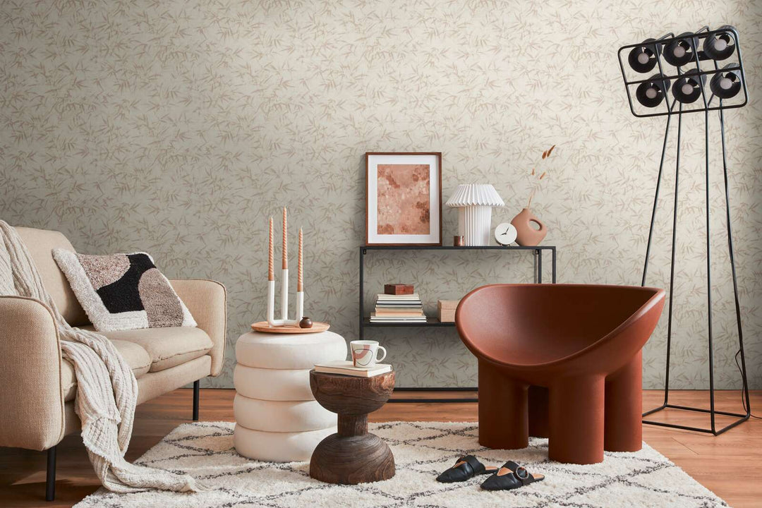 Light cream bamboo leaf pattern wallpaper in a living room interior with a light sofa, brown lounge chair, and brown wood plank flooring with a light rug