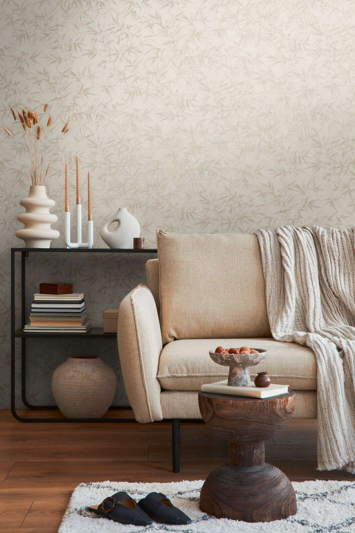 Light cream bamboo leaf pattern wallpaper in an interior with a light sofa, black shelving unit, and brown wood plank flooring with a light rug
