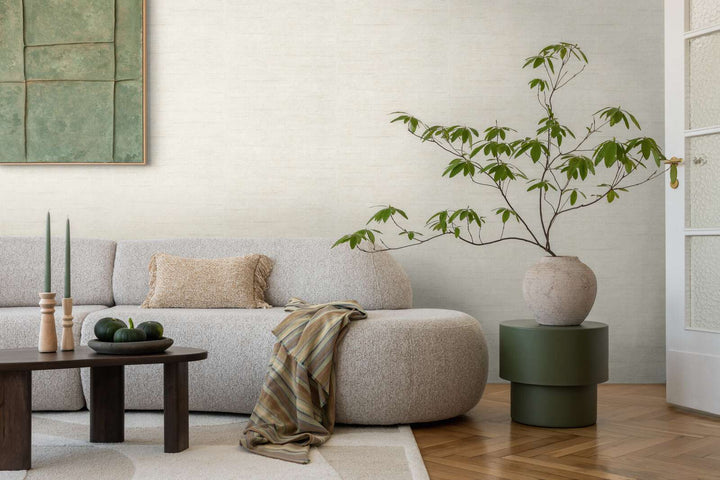Light grayish-white textured wallpaper in a living room interior with a light sofa and natural wood parquet flooring with a light rug