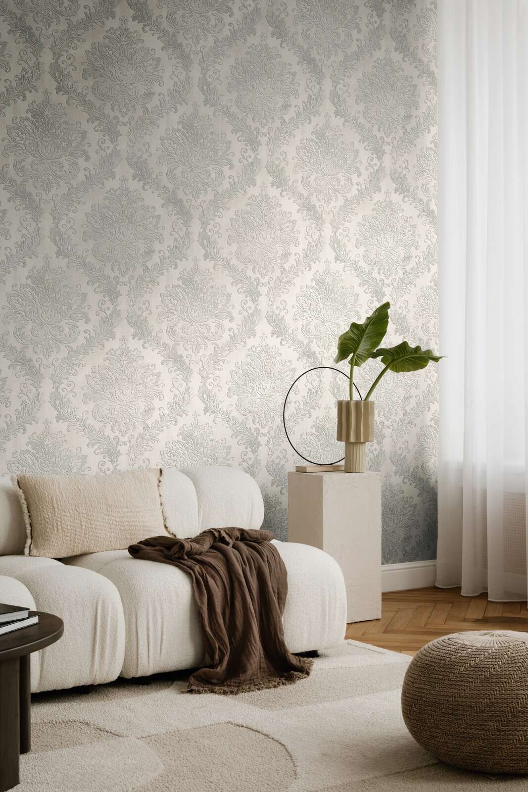 Light gray damask pattern wallpaper in a living room interior with a white sofa and natural wood parquet flooring with a light rug