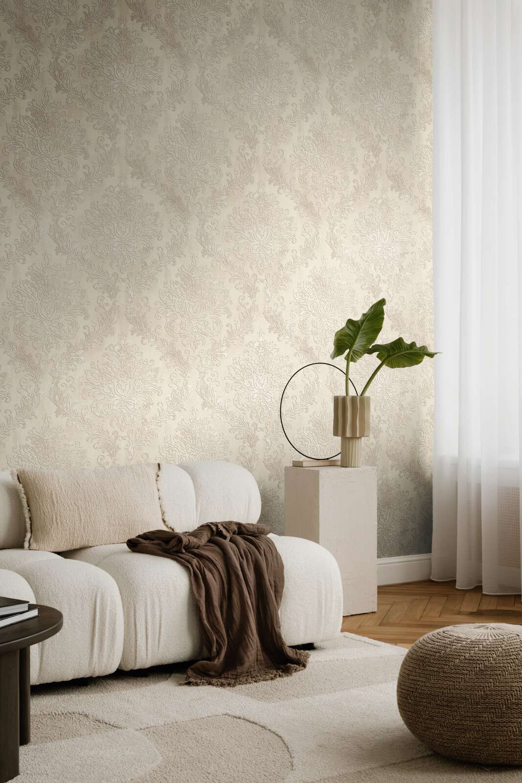 Light beige damask pattern wallpaper in a living room interior with a white sofa and natural wood parquet flooring with a light rug