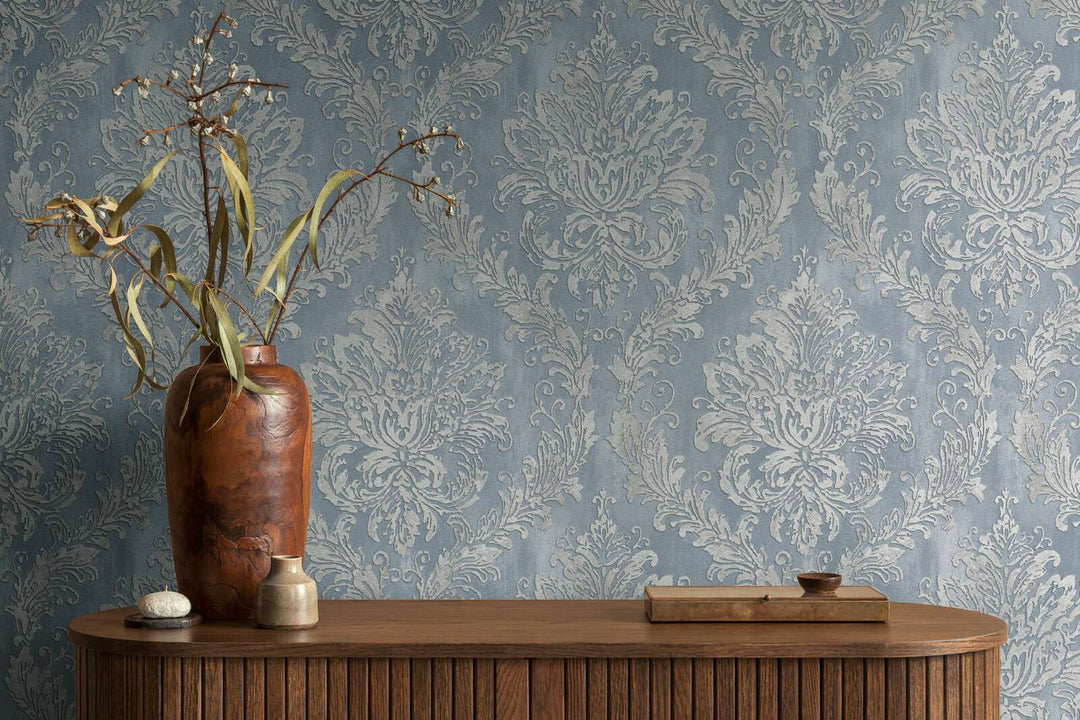 Bluish-gray damask pattern wallpaper in an interior behind a wooden cabinet with a decorative wooden vase