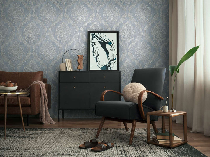 Bluish-gray damask pattern wallpaper in a living room interior with a black lounge chair, black dresser, and brown wood floor with a rug