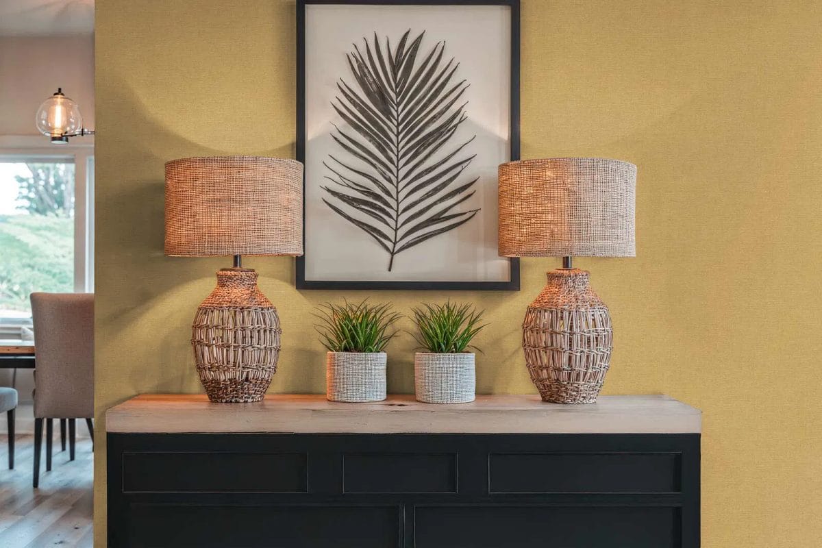 Dzeltenas spīdīgas tapetes ar dabisku tekstila dizainu saulainā viesistabas interjerā. SKU: 3012157, AS Creation.