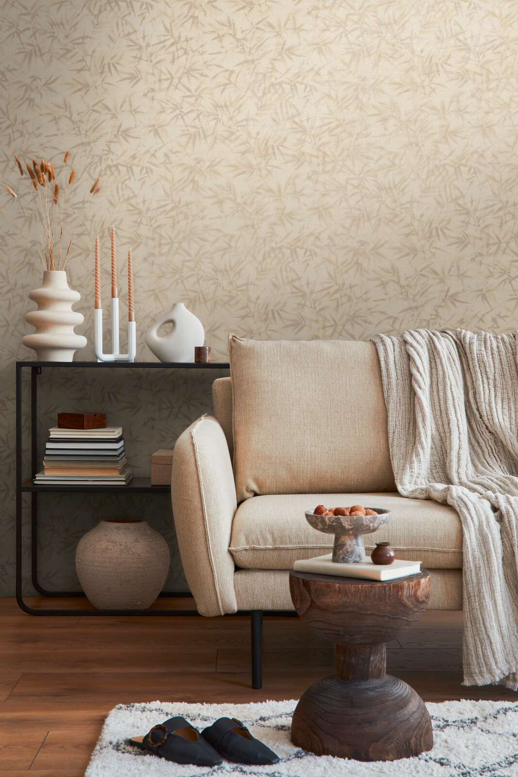 Light beige bamboo leaf pattern wallpaper in an interior with a light sofa, black shelving unit, and brown wood floor with a light rug