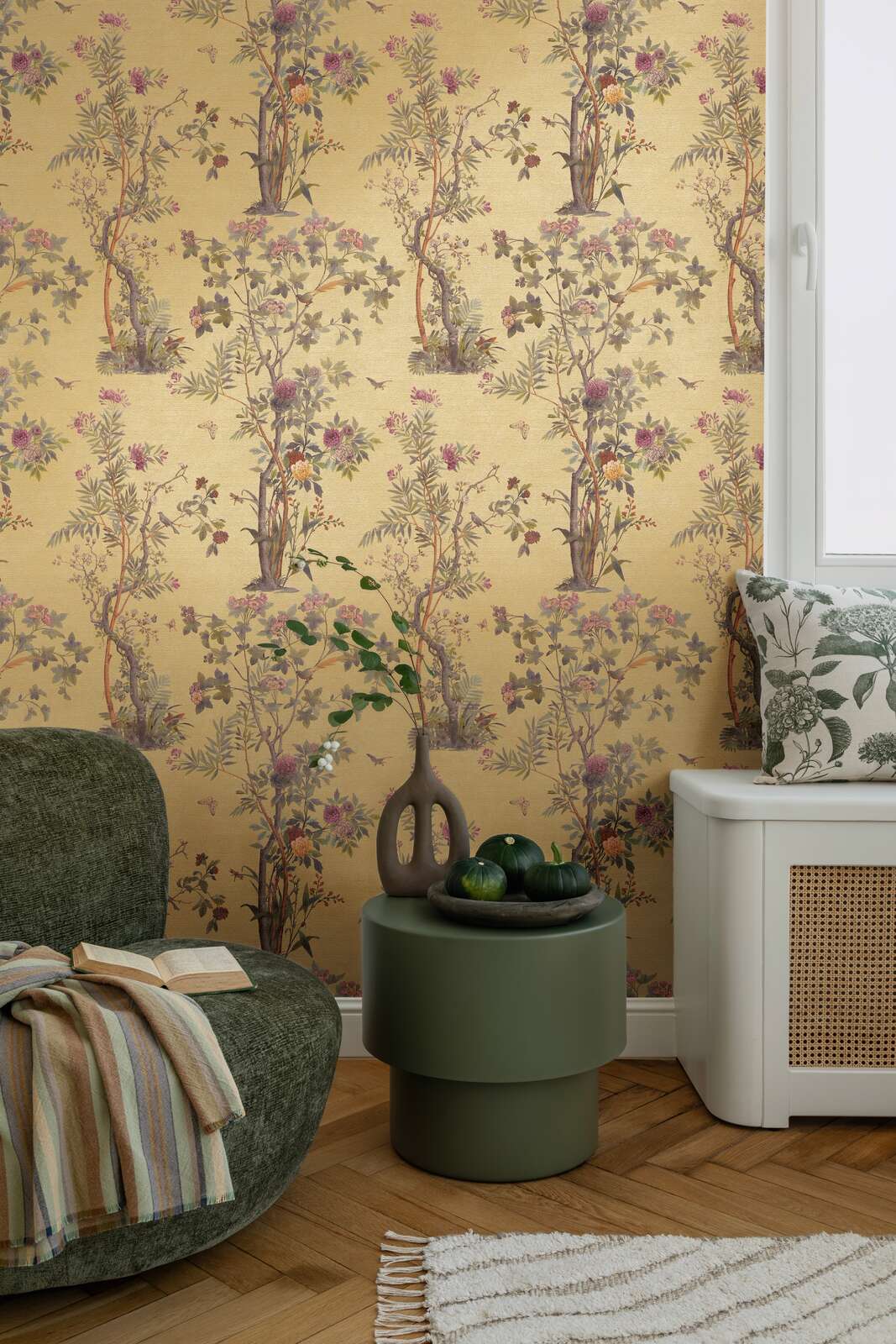 Golden-yellow illustrated nature motif wallpaper in an interior with a green lounge chair, round side table, and natural wood parquet flooring with a rug