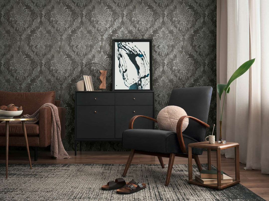 Dark gray damask pattern wallpaper in a living room interior with a black lounge chair, black dresser, and brown wood floor with a rug