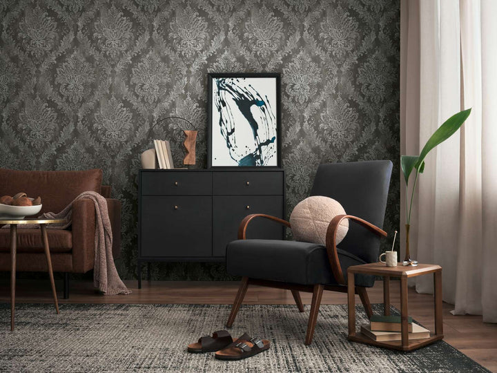 Dark gray damask pattern wallpaper in a living room interior with a black lounge chair, black dresser, and brown wood floor with a rug