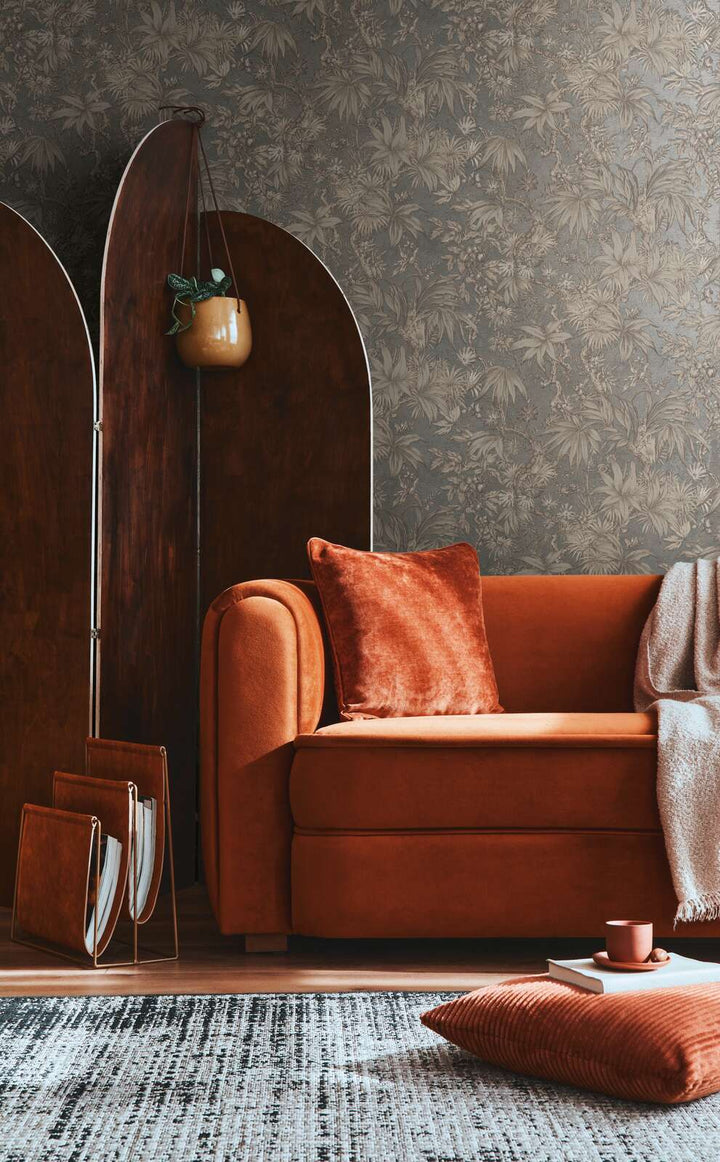 Dark grayish-brown botanical pattern wallpaper in a living room interior with a terracotta sofa and natural wood plank flooring with a rug