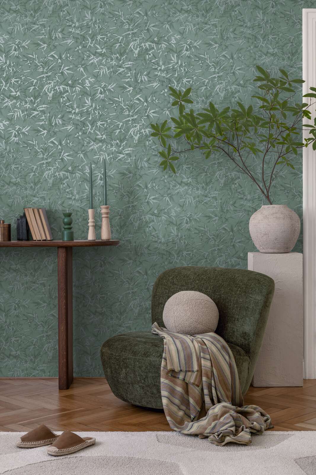 Green bamboo leaf pattern wallpaper in an interior with a green lounge chair, decorative plant in a vase, and natural wood parquet flooring with a light rug