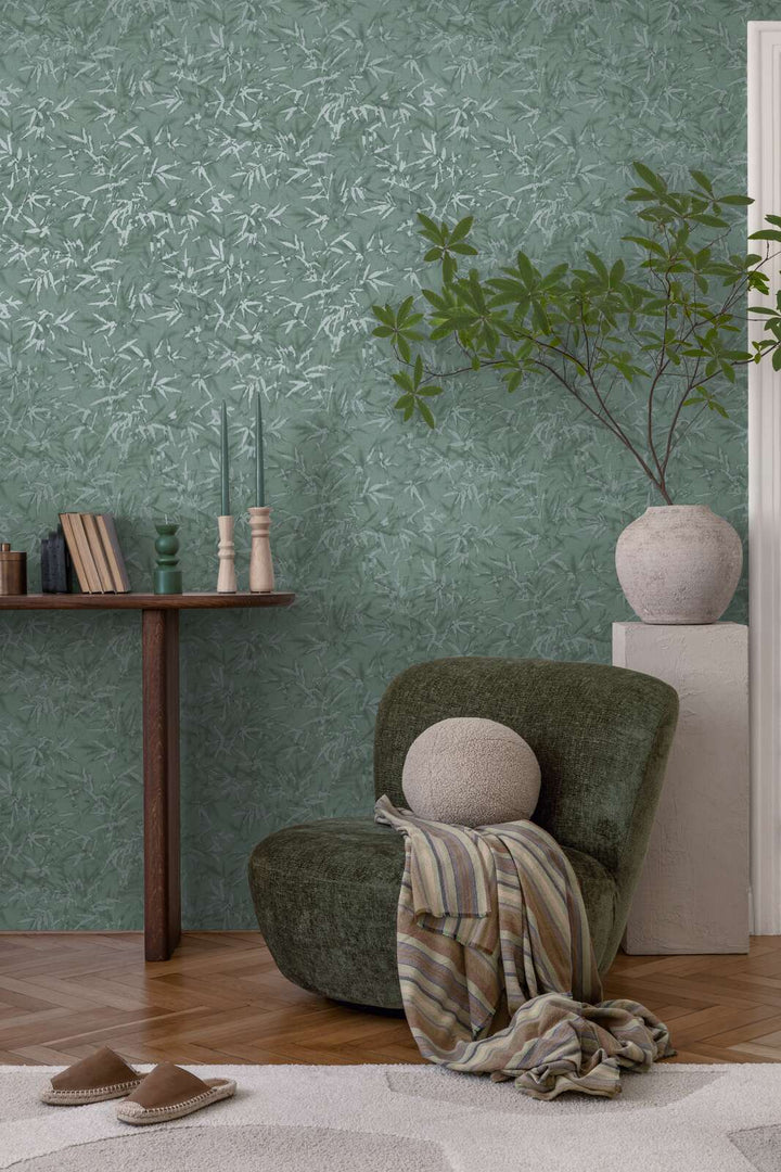 Green bamboo leaf pattern wallpaper in an interior with a green lounge chair, decorative plant in a vase, and natural wood parquet flooring with a light rug