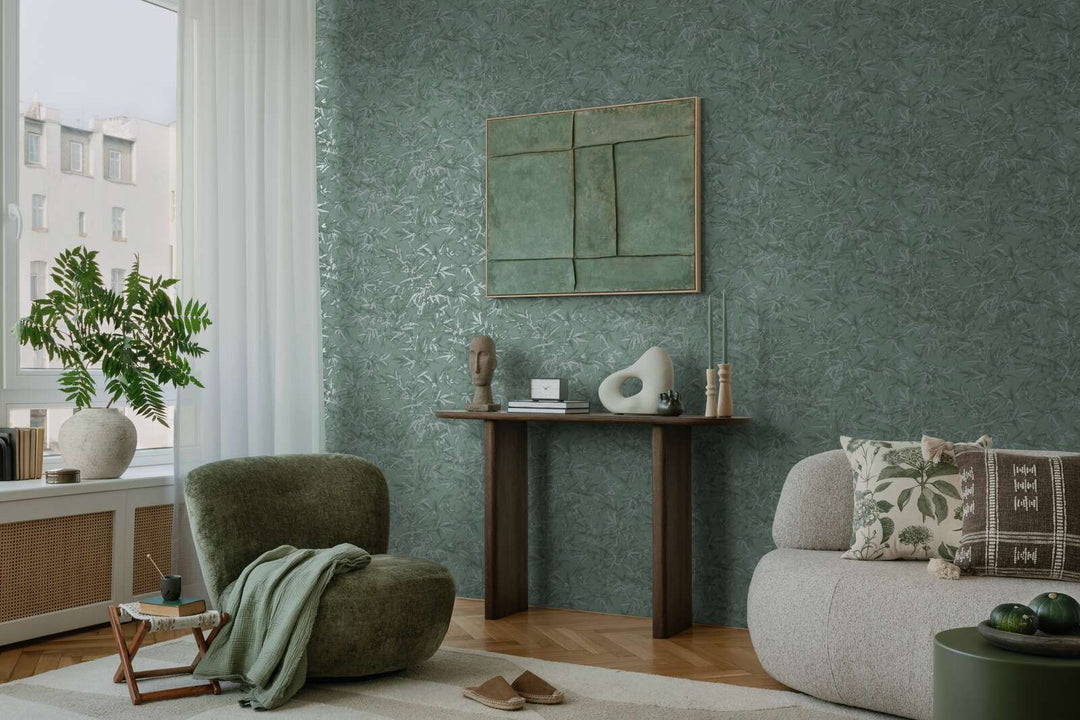 Green bamboo leaf pattern wallpaper in a living room interior with a green lounge chair, console table, and natural wood parquet flooring with a light rug