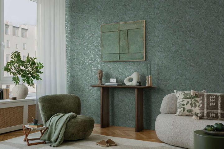 Green bamboo leaf pattern wallpaper in a living room interior with a green lounge chair, console table, and natural wood parquet flooring with a light rug
